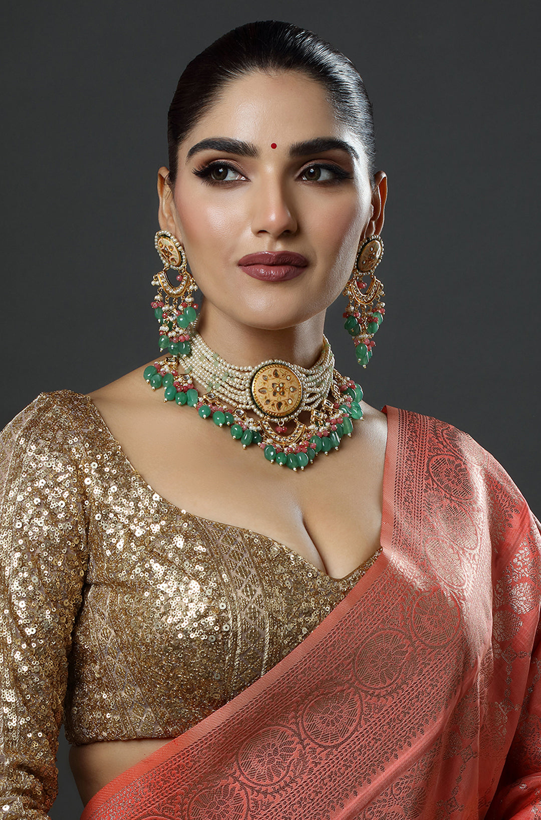 Woman wearing traditional jewelry and a saree against a dark background
