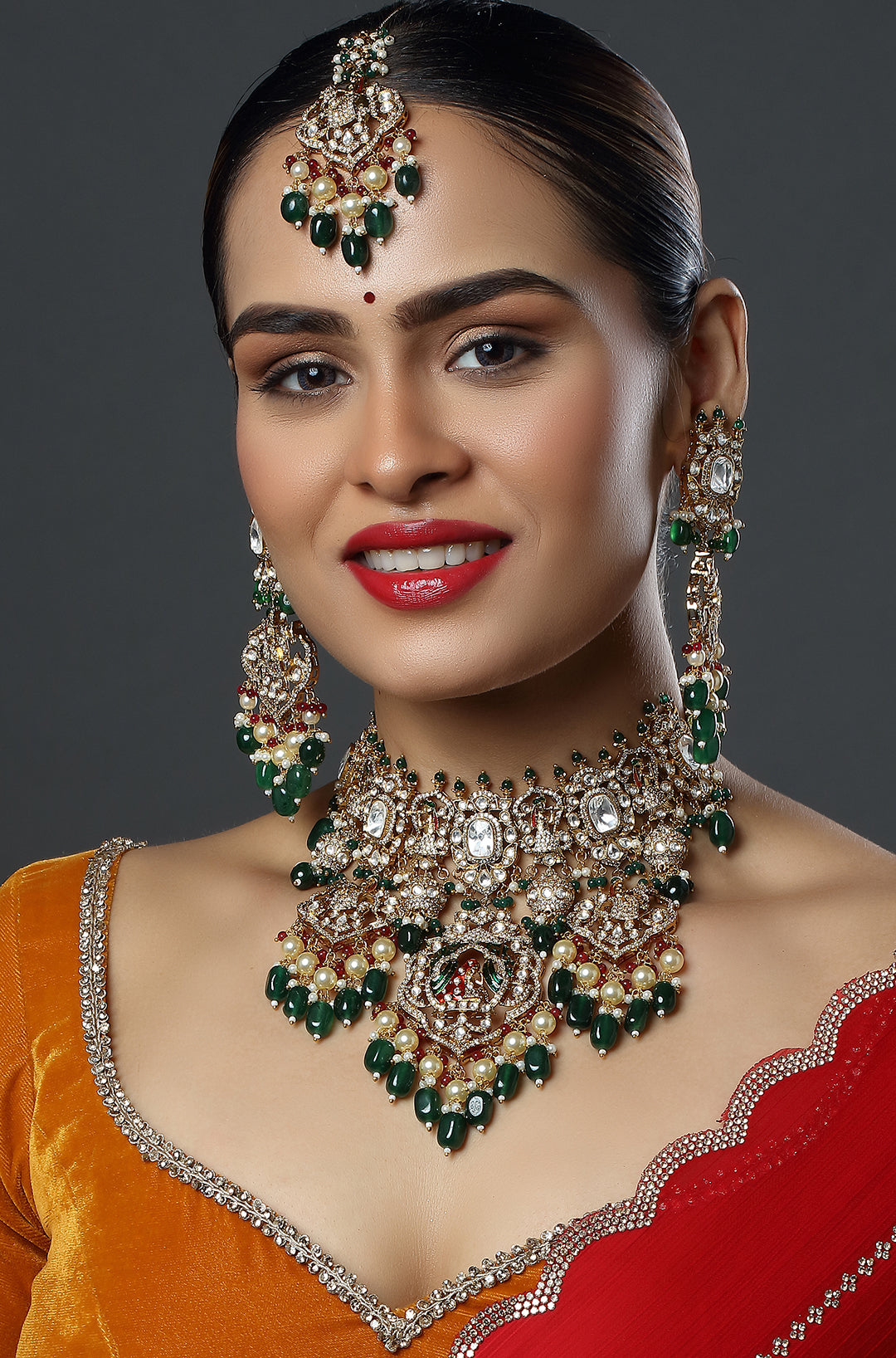 Woman wearing elaborate jewelry set with green and gold accents on a dark background