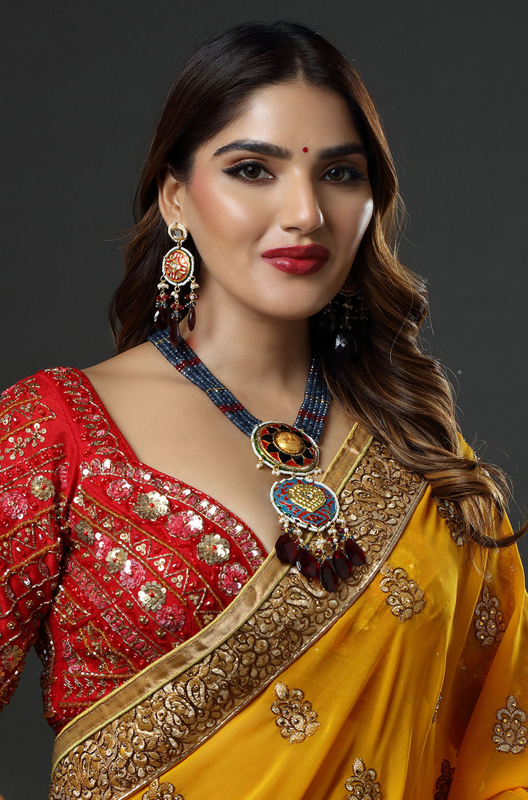 Woman wearing a red and yellow saree with jewelry on a dark background
