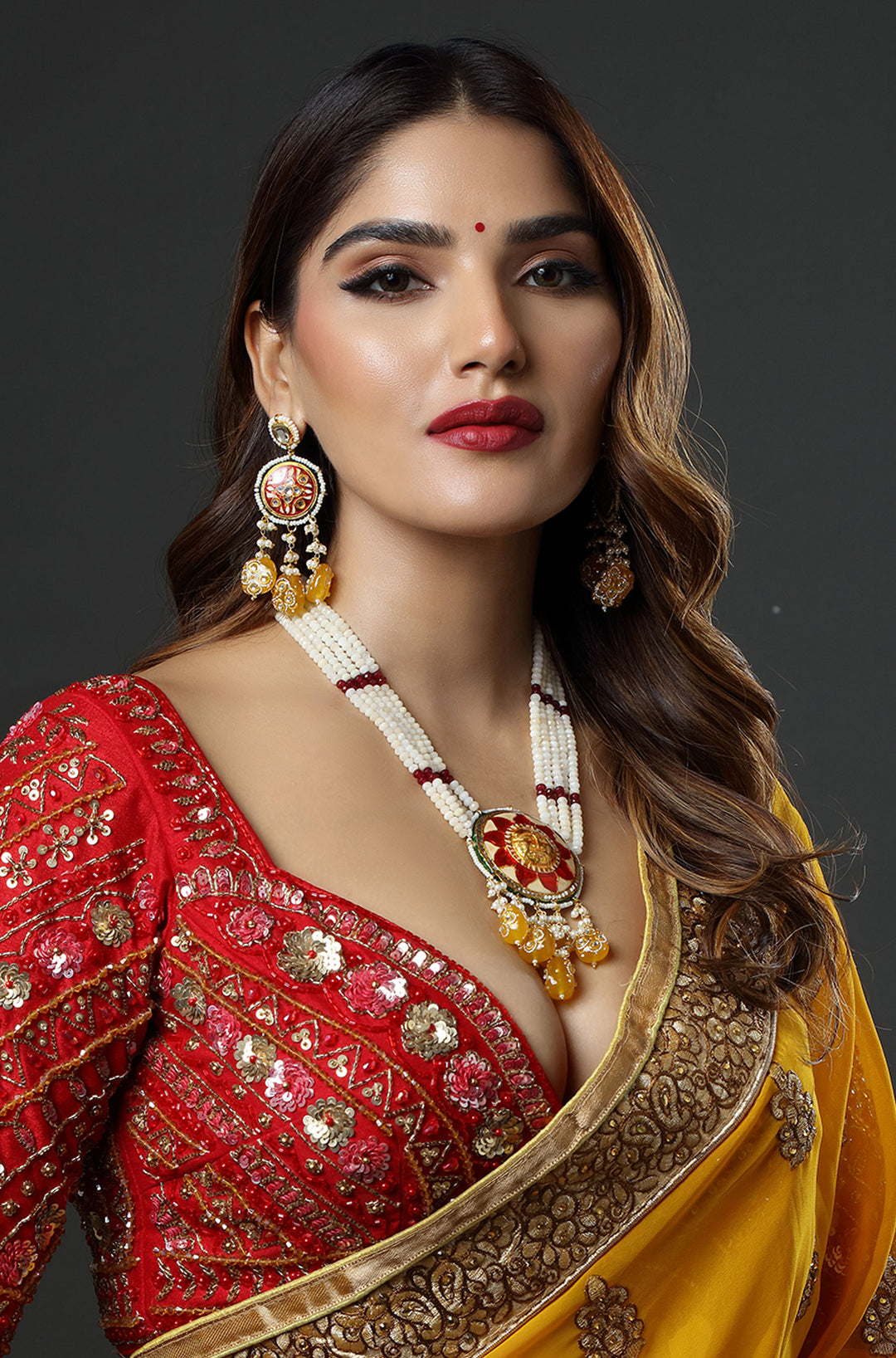 Woman wearing a red and yellow traditional outfit with jewelry on a dark background
