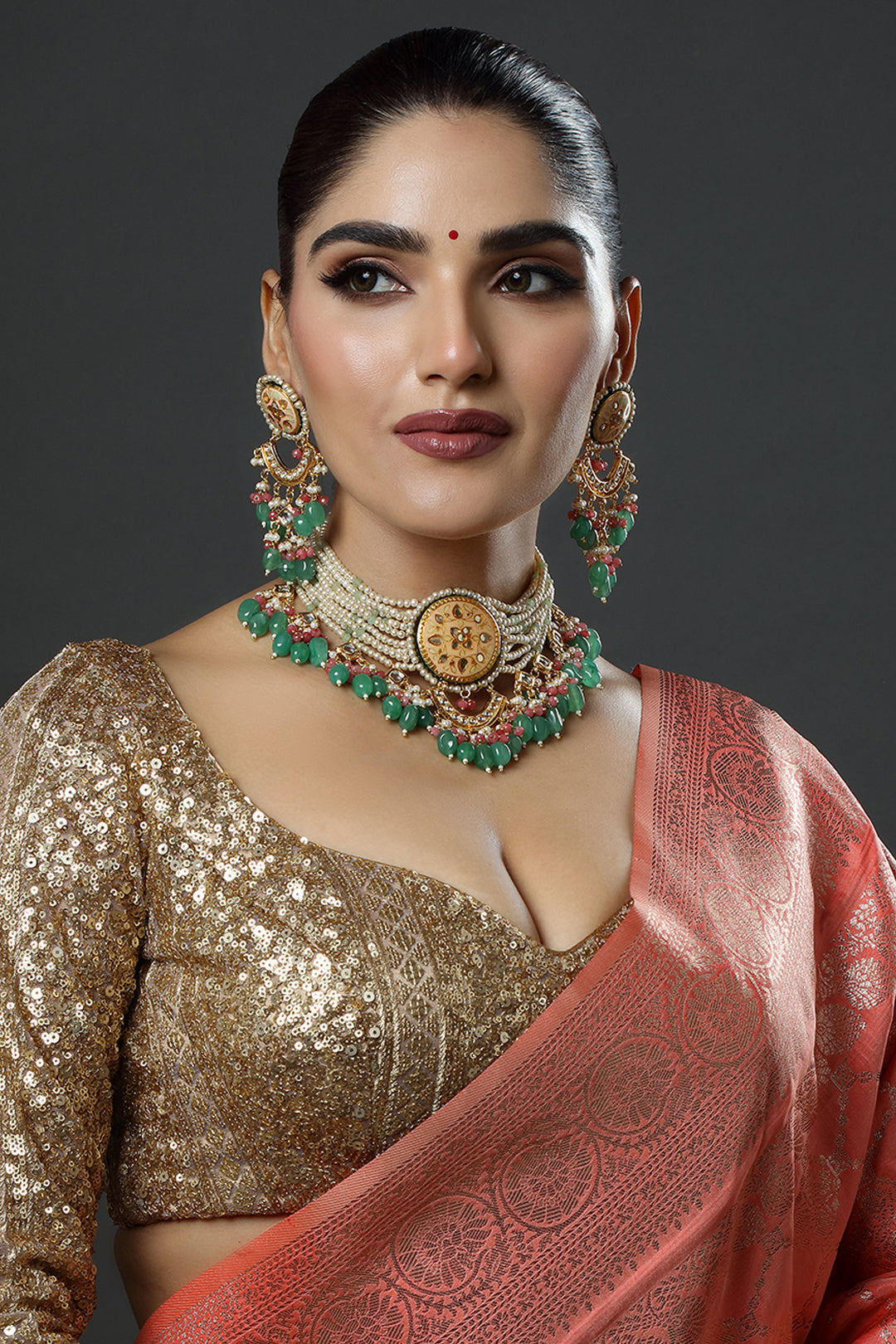 Woman wearing traditional jewelry and a saree against a dark background