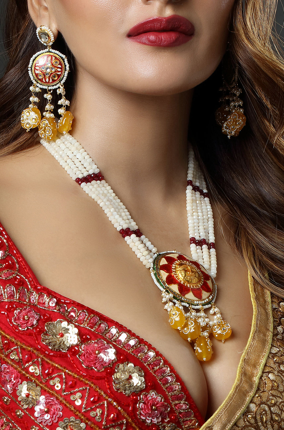 Close-up of a woman wearing a red saree with gold jewelry, including earrings and a necklace.