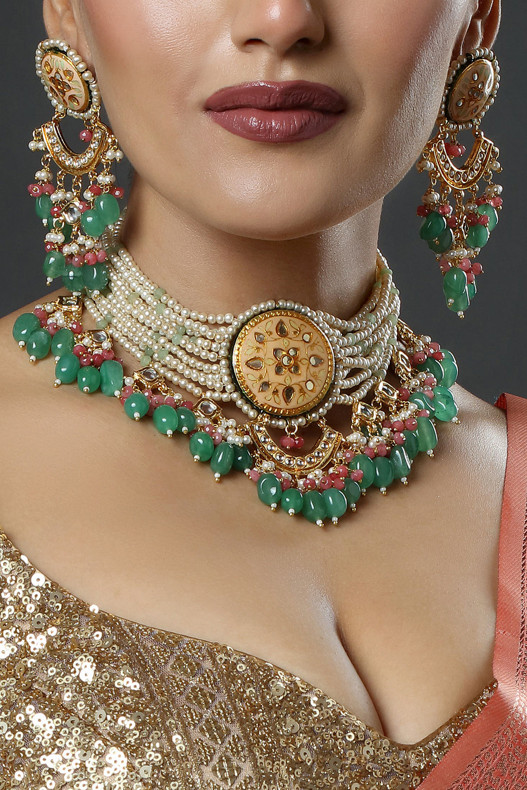 Close-up of a person wearing an elaborate gold and green jewelry set with a neutral background