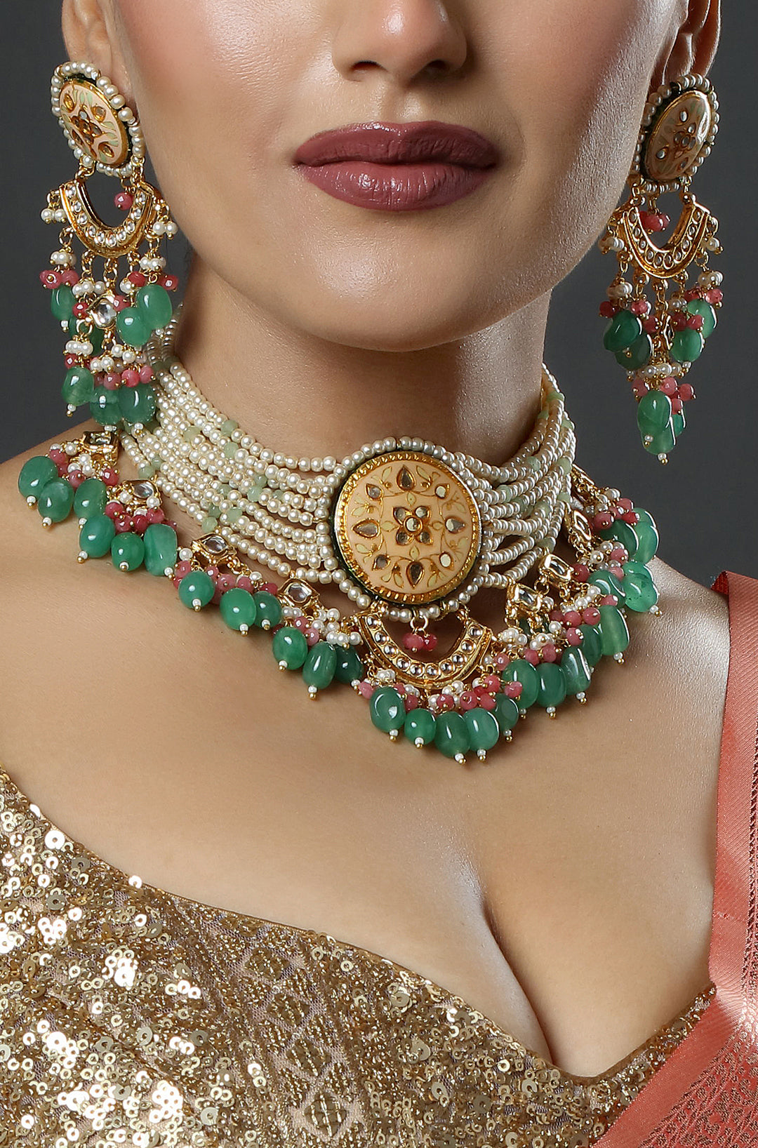 Close-up of a person wearing an elaborate gold and green jewelry set with a neutral background