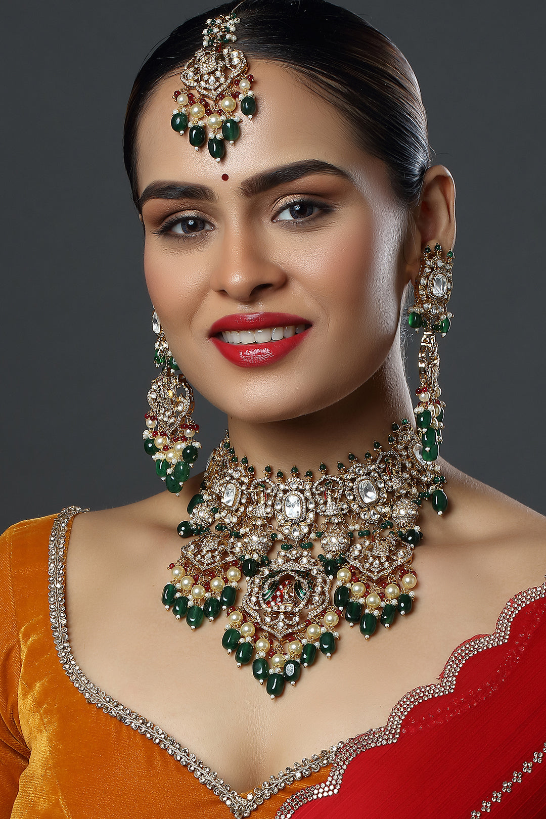 Woman wearing elaborate jewelry set with green and gold accents on a dark background