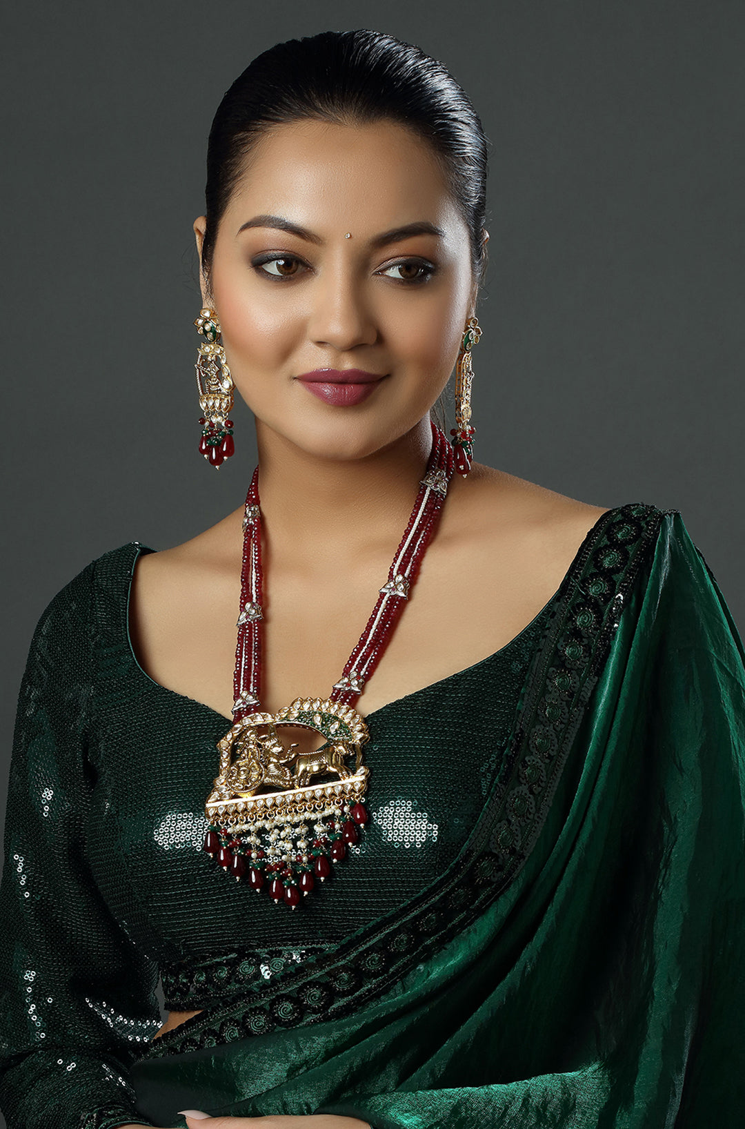 Woman wearing a green saree with a large necklace against a dark background