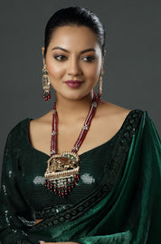 Woman wearing a green saree with a large necklace against a dark background